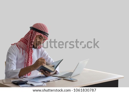 Picture of Arabian handsome man reading the books with laptop computer on the desk/Isolated on gray background