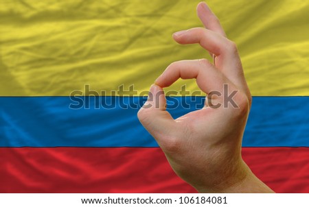 man showing excellence or ok gesture in front of complete wavy colombia national flag of  symbolizing best quality, positivity and success