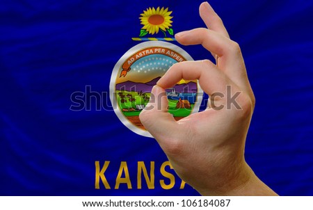 man showing excellence or ok gesture in front of complete wavy american state flag of kansas symbolizing best quality, positivity and success