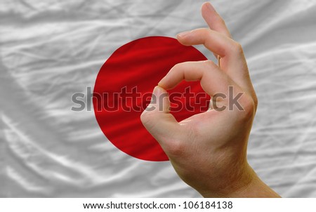 man showing excellence or ok gesture in front of complete wavy japan national flag of  symbolizing best quality, positivity and success