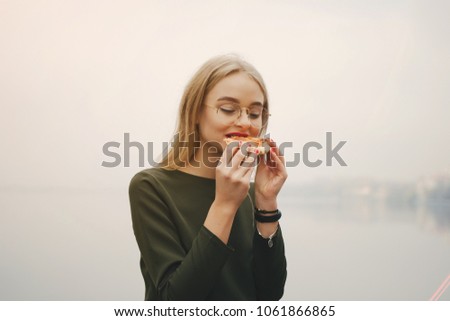 young and stylish girl walking in the autumn park near water and eat pizza