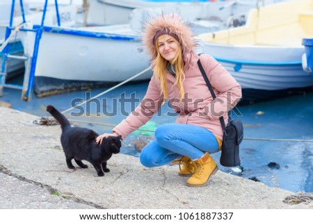 Girl with a black cat on the pier. Homeless black cat