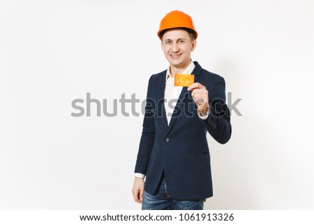Young handsome smiling businessman in dark suit, protective construction orange helmet holding credit card isolated on white background. Male worker for advertisement. Business, working concept