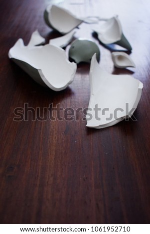 Shards of a ceramic grey object on a dark wood background.