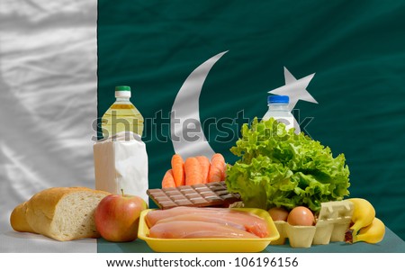 complete national flag of pakistan covers whole frame, waved, crunched and very natural looking. In front plan are fundamental food ingredients for consumers, symbolizing consumerism