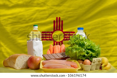 complete american state flag of new mexico covers whole frame, waved, crunched and very natural looking. In front plan are fundamental food ingredients for consumers, symbolizing consumerism