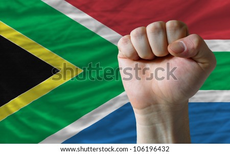 complete national flag of south africa covers whole frame, waved, crunched and very natural looking. In front plan is clenched fist symbolizing determination