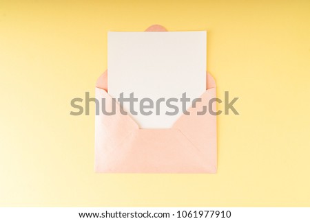 Minimal composition with a pink envelope, white blank card on a yellow pastel background. Mockup with envelope and blank card. Flat lay. Top view.