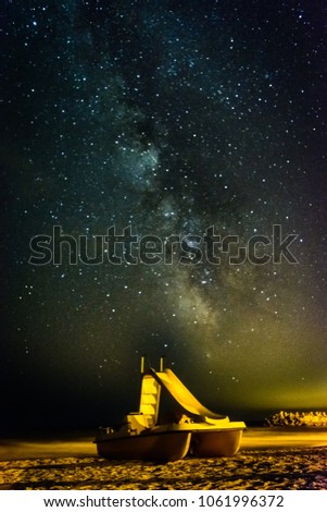 Night photo of a yellow paddle boat on the sand of the beach with the galaxy of the Milky Way centered over it