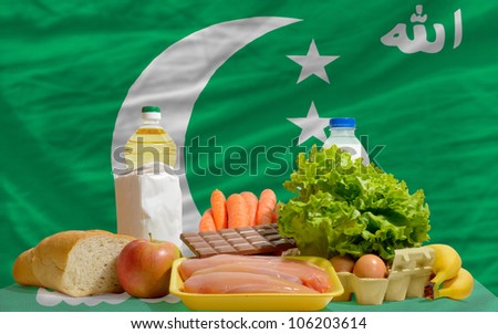 complete national flag of comoros covers whole frame, waved, crunched and very natural looking. In front plan are fundamental food ingredients for consumers, symbolizing consumerism
