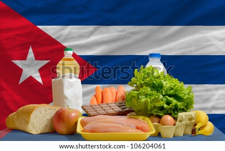 complete national flag of cuba covers whole frame, waved, crunched and very natural looking. In front plan are fundamental food ingredients for consumers, symbolizing consumerism