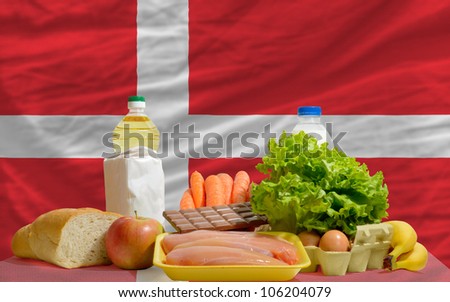 complete national flag of denmark covers whole frame, waved, crunched and very natural looking. In front plan are fundamental food ingredients for consumers, symbolizing consumerism