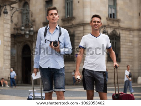 positive american male couples with travel bags walking the city
 