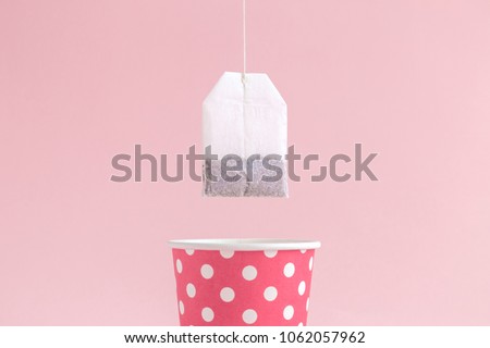 Dipping tea bag into paper cup polka design on pastel pink background minimal creative concept.