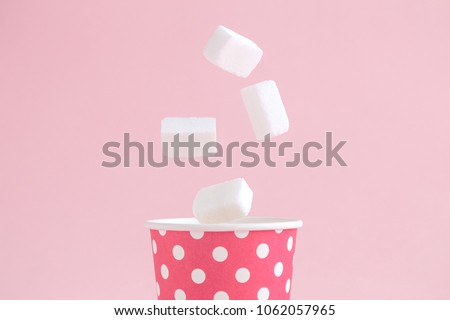 Sugar cubes falling into paper cup polka design against pastel pink background minimal creative concept. Royalty-Free Stock Photo #1062057965