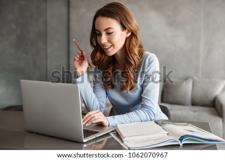 Portrait of a pretty young woman studying while sitting at the table with laptop computer and notebook at home Royalty-Free Stock Photo #1062070967