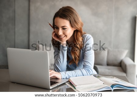 Portrait of a beautiful young woman studying while sitting at the table with laptop computer and notebook at home Royalty-Free Stock Photo #1062070973