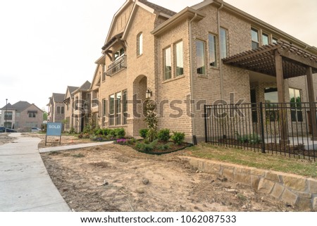 Row of newly built detached single-family homes and sold out sign. Medium size multiple lot properties in new-established community, construction zone with unfinished landscape Irving, Texas, USA