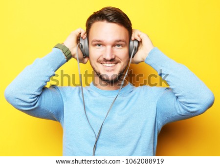 lifestyle and people concept: Happy young man listening to music with headphones over yellow background close uo