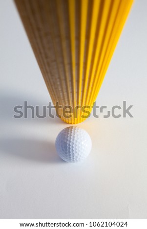 Corrugated yellow paper roll and golf ball on the white desk. Exclamation mark.