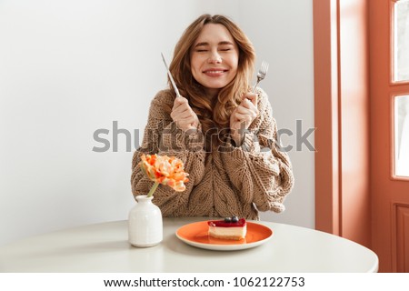 Portrait of an excited woman in sweater getting ready to eat cheesecake on a plate at the table Royalty-Free Stock Photo #1062122753