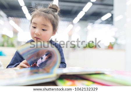 A little asian girl reading in the library