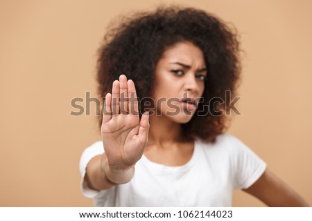 Close up portrait of a serious young african woman showing stop gesture with her palm isolated over beige background