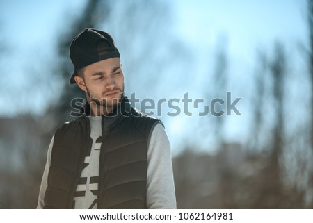 Portrait of a young cute white guy in a black cap and waistcoat posing on the street.