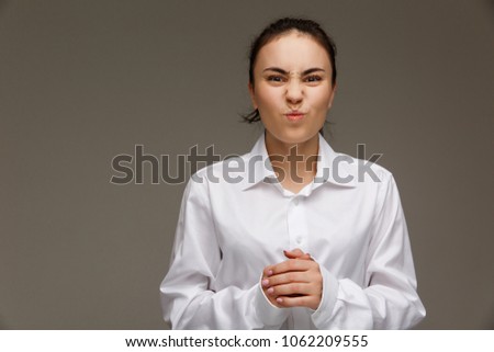 Beautiful girl in a white shirt shows emotions - dislike. On a light background.