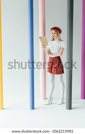 Attractive young woman reading book and posing by colorful pillars