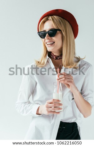 Attractive young woman in sunglasses drinking milk isolated on grey