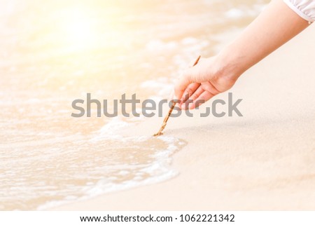 Hand hold stick by finger and writting on sand and water flow.