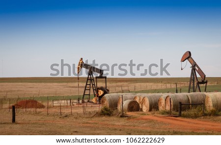 A scene from rural Oklahoma. Oil pumps and hay bales in the prairie.
