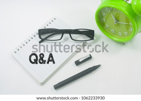 alarm clock,glasses,pen and notebook written Q and A over white background