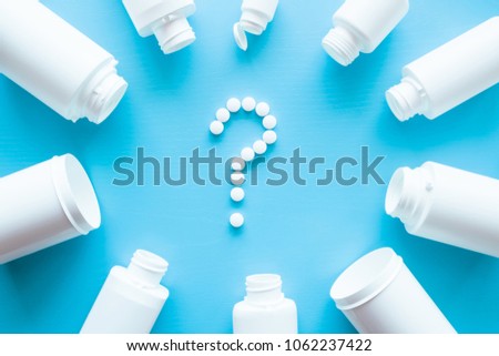 Question sign created from white pills. White bottles on blue background. The choice of vitamins or pills for good health. Medical, pharmacy and healthcare concept. Royalty-Free Stock Photo #1062237422