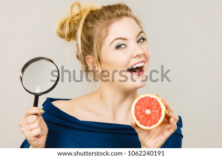 Blonde woman holding magnifying glass investigating and looking closely fruit orange or grapefruit