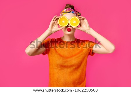 Young woman with red lips on vibrant pink background holds cut orange in her hands near eyes and kissing. Concept of healthy food and lifestyle Royalty-Free Stock Photo #1062250508