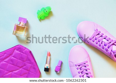 Flat lay fashion photo. Purple cosmetic bag, summer perfume, pink lipstick, nail polish, violet color sneakers and green crocodile toy. Sport chic style