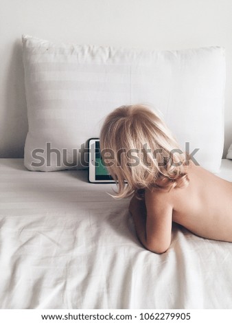Back view blonde baby watch cartoons on laptop in light room