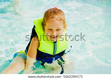 Smiling little blonde girl in a life vest in the swimming pool Royalty-Free Stock Photo #1062284171