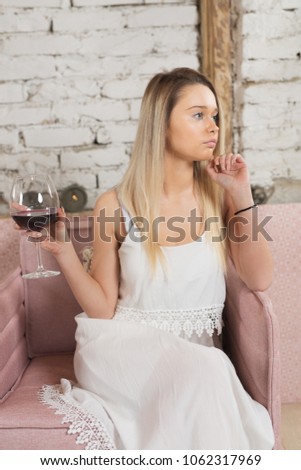 A young woman sits in her armchair and drinks red wine