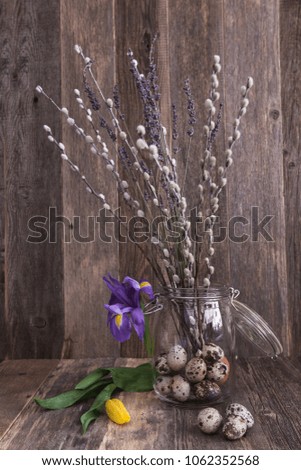 Easter picture: glass jar full of quail eggs with iris flower and willows at the wooden background