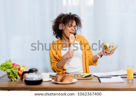 expressive young woman listening music and preparing salad at kitchen Royalty-Free Stock Photo #1062367400