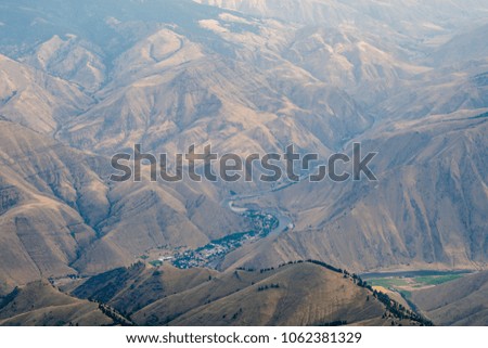Aerial shot of a green summit in the foreground with dry brown mountains and river valley in the hazy distance.