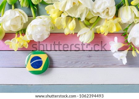Brasilian flag printed on button badge and beautiful flowers on striped wooden background.  Royalty-Free Stock Photo #1062394493