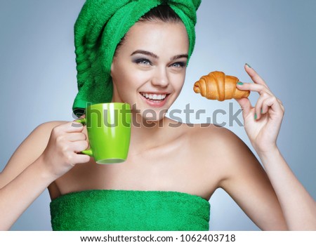 Good morning! Attractive girl in green towels with cup of coffee and croissant on blue background.