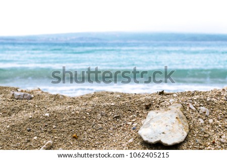 Sunny sandy beach, closeup of a rock with blurry sea in the background, shallow depth of field