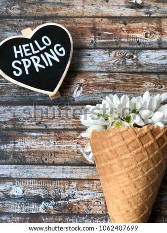 waffle cone with snowdrops and hello spring heart chalkboard on wooden background. spring chalkboard for your text. 