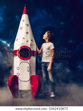 Boy is standing near toy rocket on space background with smoke at the bottom.