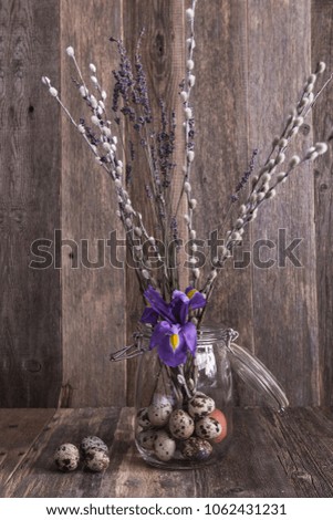 Easter picture: glass jar full of quail eggs with iris flower and willows at the wooden background